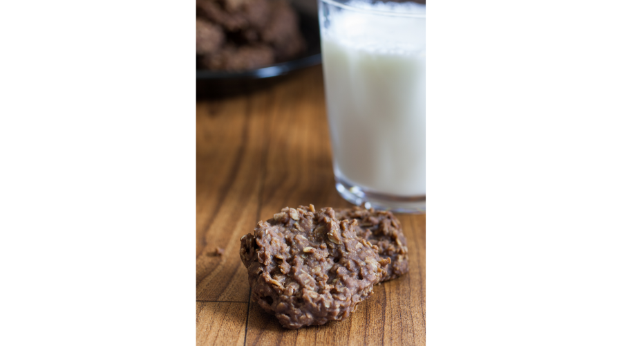 two chocolate oatmeal cookies sitting on a wooden table with glass of milk